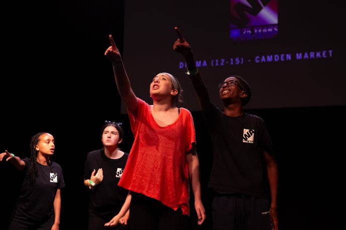 Group of four kids performing with a dark background with the lead wearing a red tshirt and the rest wearing black