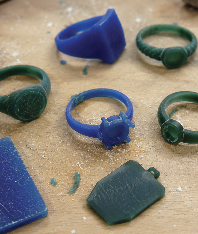 Blue and green wax ring molds on a sandy surface, used for jewelry making and casting.