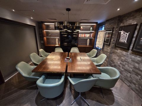 A modern conference room with a wooden table, ten teal chairs, shelves with books and decor, wall art, and dim lighting.