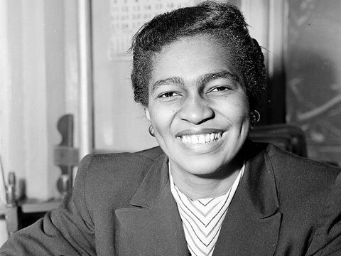 Woman smiles to camera with hair pulled back and wearing smart coat