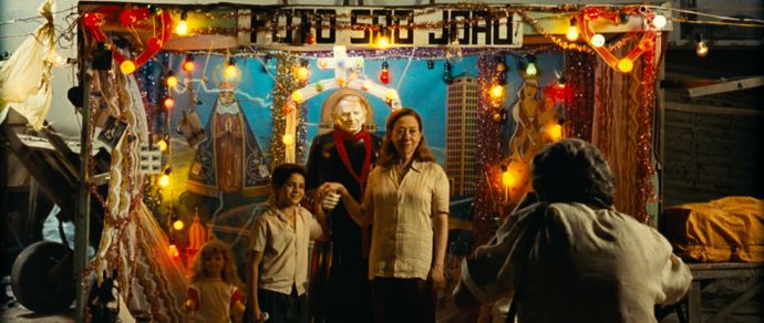 A family poses for a photo in front of a colorful, decorated backdrop with lights and religious imagery. A photographer captures the moment.