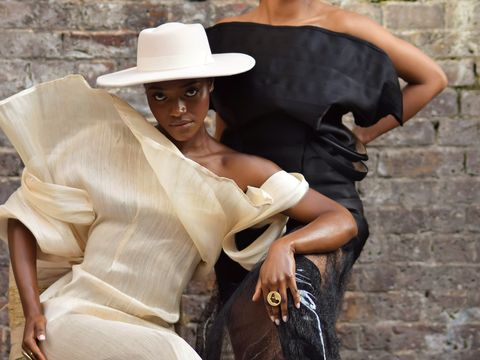 Two fashionably dressed people pose against a brick wall, showcasing elegant, contemporary clothing and accessories.
