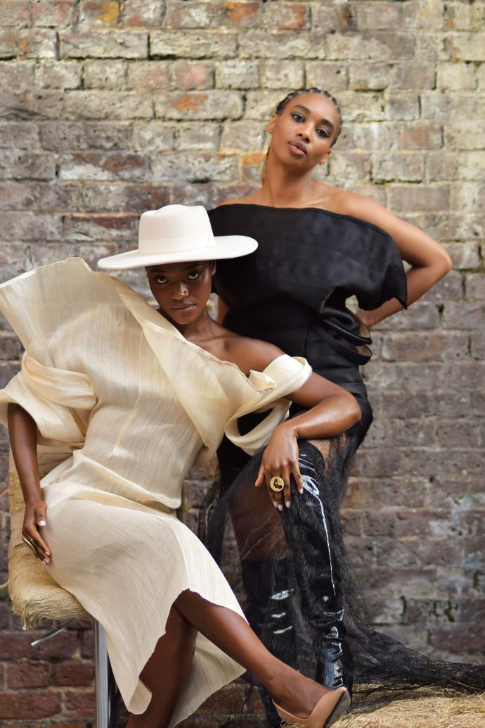 Two fashionably dressed people pose against a brick wall, showcasing elegant, contemporary clothing and accessories.