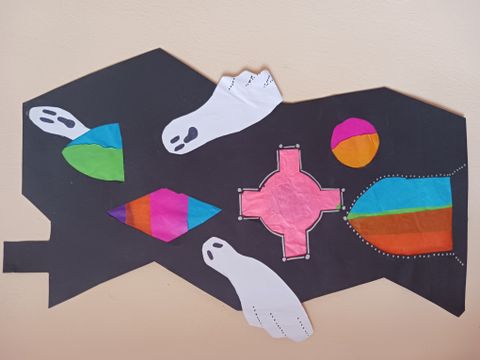 A black paper cut-out shaped like a house, decorated with colourful tissue paper shapes and two white paper ghosts with black facial features.