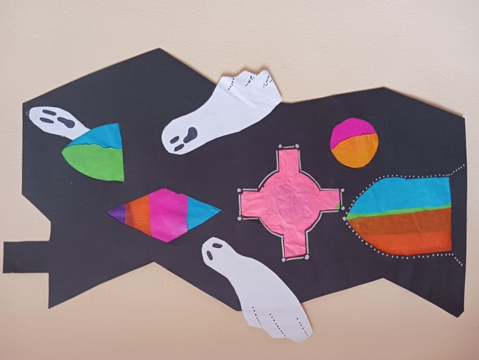 A black paper cut-out shaped like a house, decorated with colourful tissue paper shapes and two white paper ghosts with black facial features.