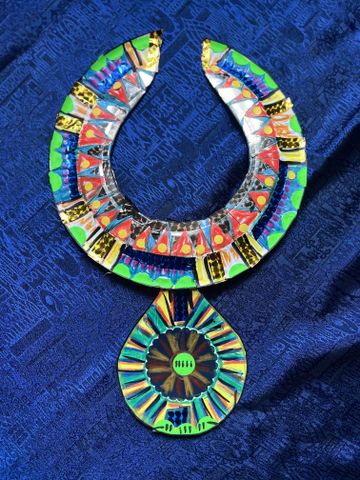 Colorful, intricate necklace with geometric patterns on a textured blue fabric background.