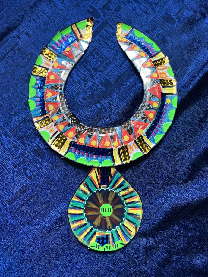 Colorful, intricate necklace with geometric patterns on a textured blue fabric background.