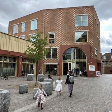 Modern brick community centre with courtyard where people and children gather and walk outside.