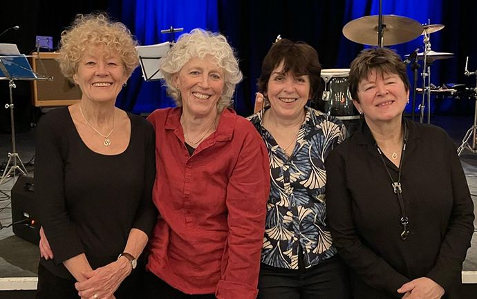 Four people standing together on a stage with musical instruments in the background, smiling at the camera.