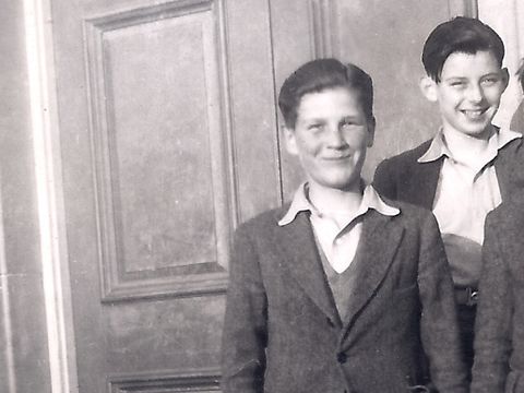 Three boys in suits stand smiling in front of a wooden door, with one boy laughing energetically.