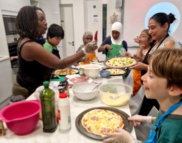 People of various ages and backgrounds are joyfully assembling pizzas together in a kitchen.