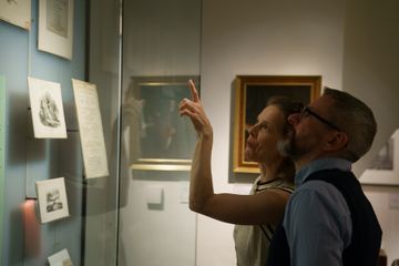 2 individuals look at artwork through glass