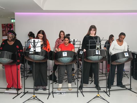 Group of people stand in front of steel pans playing against white background