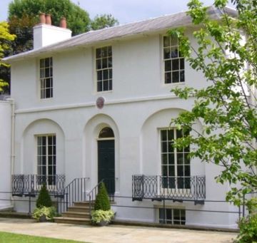 A white two-story house with a slate roof, arched windows, and a small front lawn with trees and shrubs.
