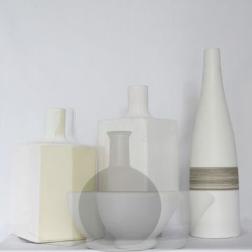 Minimalist arrangement of white and cream vases with geometric shapes against a plain background.