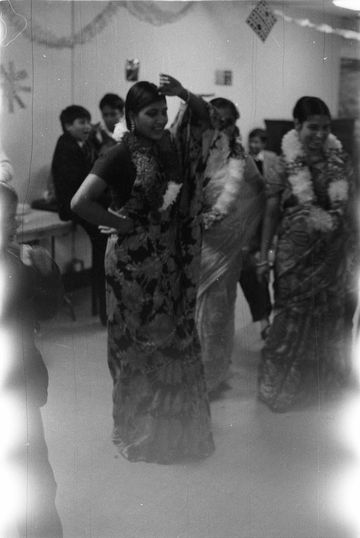 Black and white aged photo of people in traditional dress smiling indoors with decorations in background