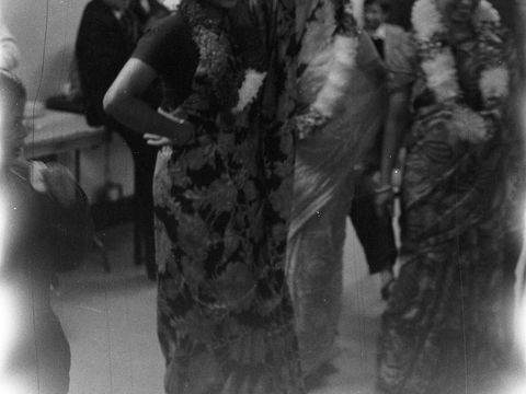 Black and white aged photo of people in traditional dress smiling indoors with decorations in background