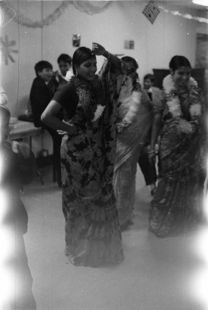 Black and white aged photo of people in traditional dress smiling indoors with decorations in background