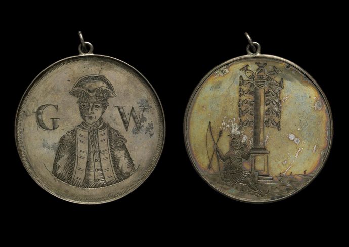Two old medallions, worn and discoloured by time, one shows a man in military uniform with letters 'G W' and the other shows a person sitting on side holding bow and arrow