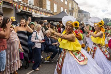 People wearing traditional yellow and white dress, dancing with sunflowers in hair and crowd gathering on residential street