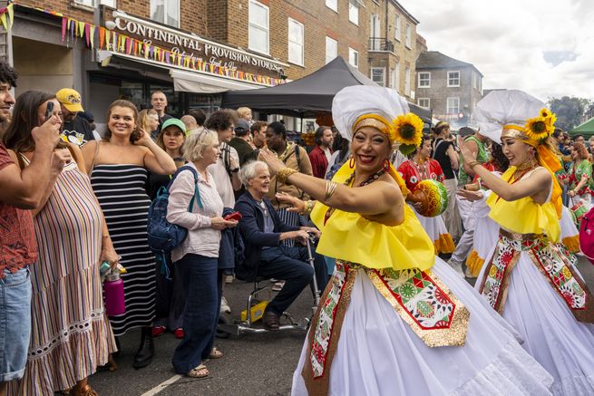People wearing traditional yellow and white dress, dancing with sunflowers in hair and crowd gathering on residential street