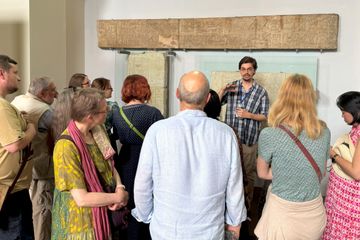 A group of people listens to a guide explaining ancient artifacts displayed on a wall in a museum setting.