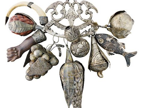 Ornate antique charm cluster featuring miniature fish, hand, horn, fruit, and decorative metal pendants.
