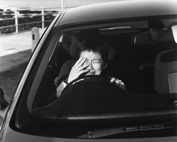 Individual sits in car whilst trying to shield themselves from the sun.