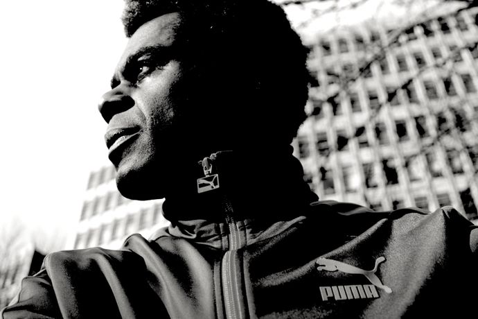 Black and white photo of person looking to distance wearing puma jacket and towerblock in background