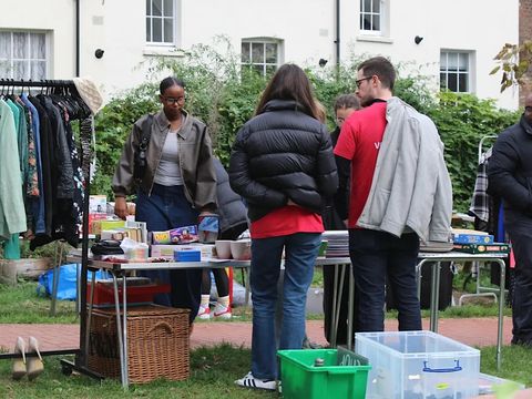 Outdoor community market with people browsing clothes, books, and household items on tables together nearby.