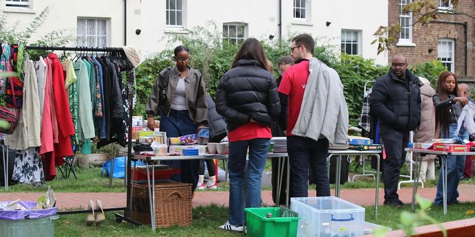 Outdoor community market with people browsing clothes, books, and household items on tables together nearby.
