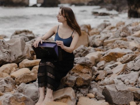 Lady with dark blonde hair sat on rocks next to a river and hills