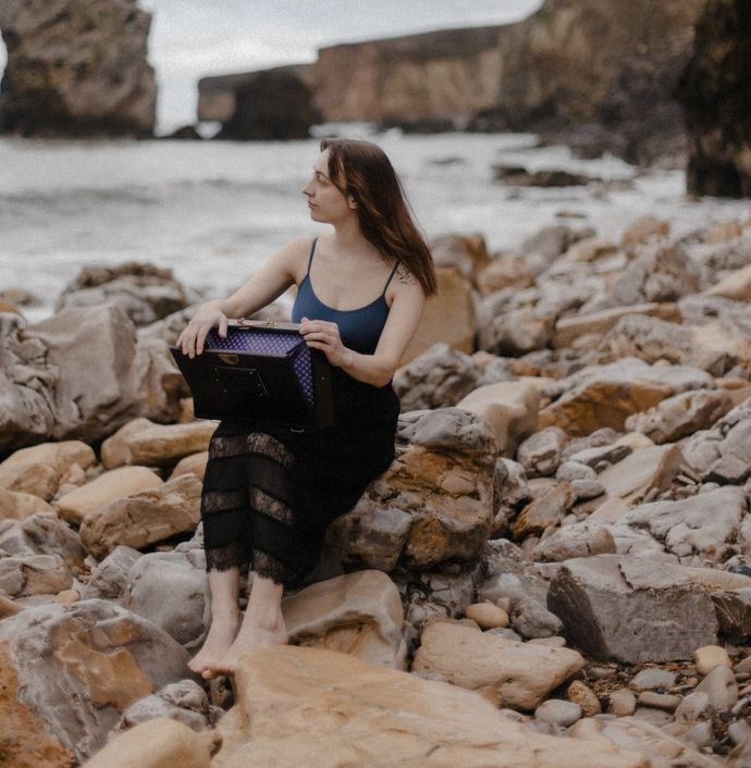 Lady with dark blonde hair sat on rocks next to a river and hills