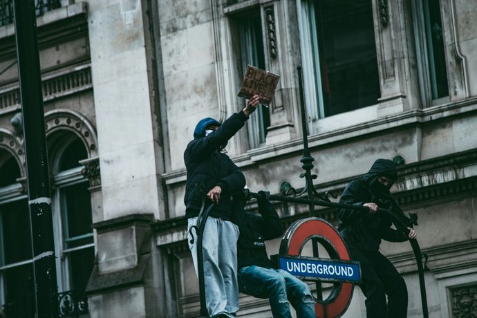 Protesters demonstrate atop a London Underground entrance holding a "Black Lives Matter" sign, against an ornate building backdrop.