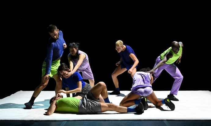 seven people wearing variations of blue, lime green and lilac tops and trouser combos move in different posed shapes