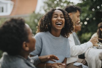 Girl laughing with curly hair, outdoors with people neraby