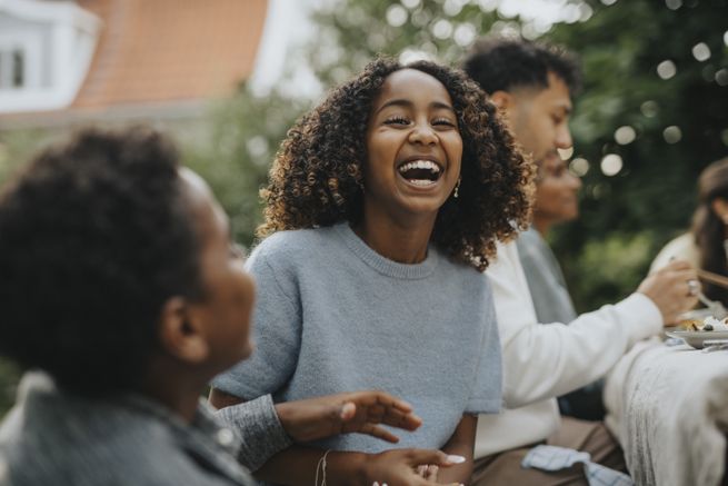 Girl laughing with curly hair, outdoors with people neraby