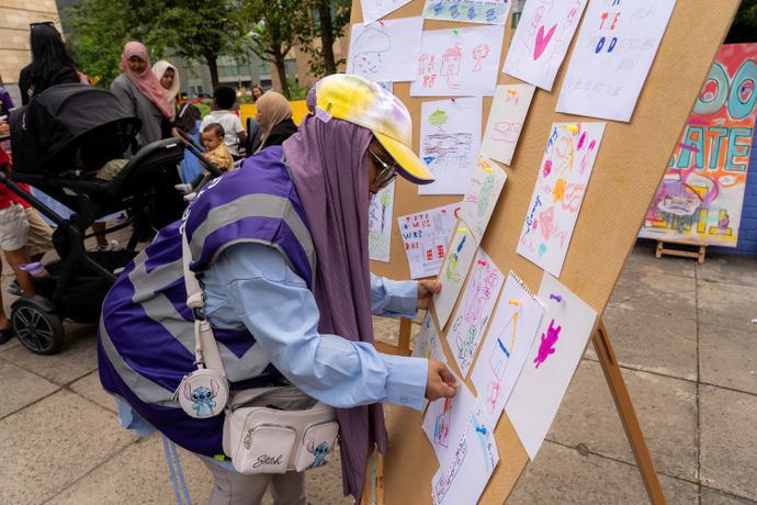 Person wearing hat and head scarf places colourful paper to board