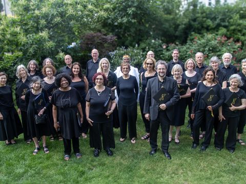 Group of people wearing black smile to camera while standing on grass with green hedges behind them