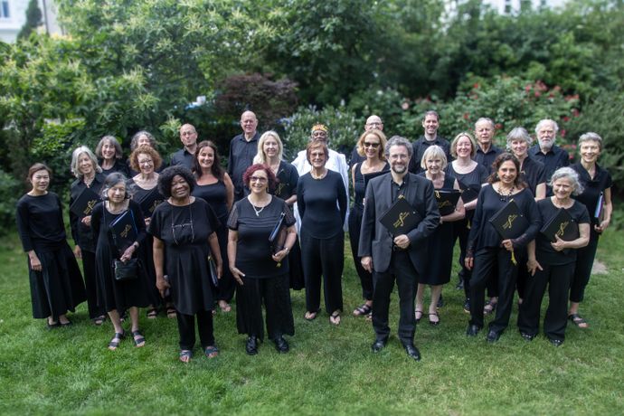 Group of people wearing black smile to camera while standing on grass with green hedges behind them