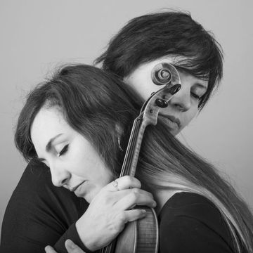 2 individuals hug each other with musical instruments in their hands