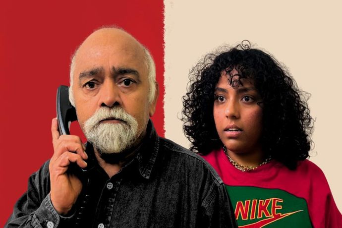 Man with white beard looks worried with hand-set phone held to ear as younger woman with shoulder-length black curly hair looks open eyed and mouthed behind him
