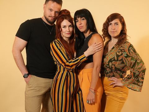 Four people in colourful smart-casual outfits standing together in front of a plain beige background
