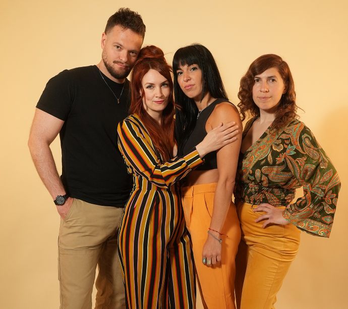 Four people in colourful smart-casual outfits standing together in front of a plain beige background