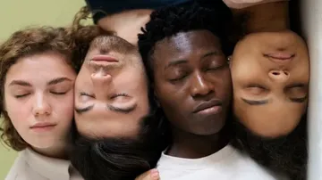 Two people wearing casual clothing are closely positioned against a light green background, with one person’s hand gently resting on the other’s shoulder.