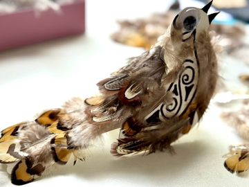A decorative bird with intricate patterns and detailed feather design, featuring brown and tan tones, sits on a light surface.