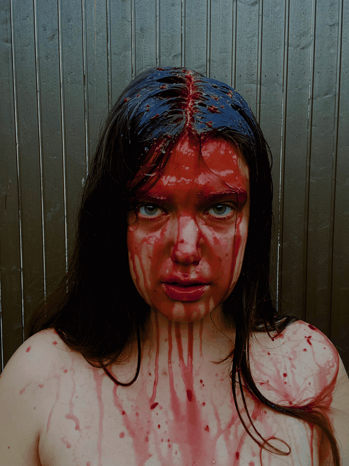 Young woman with long black hair stares to camera with red liquid all over hair and face