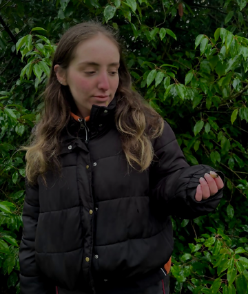 Actress stand in puffer jacket with a cigarette in hand and looking at the cigarette