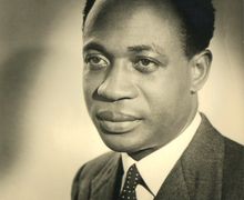 Portrait of a man in a suit and polka dot tie, looking to the side with a neutral expression, set against a plain background.