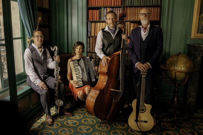 Four musicians in vintage attire pose in a library, holding instruments including a clarinet, accordion, double bass, and guitar.